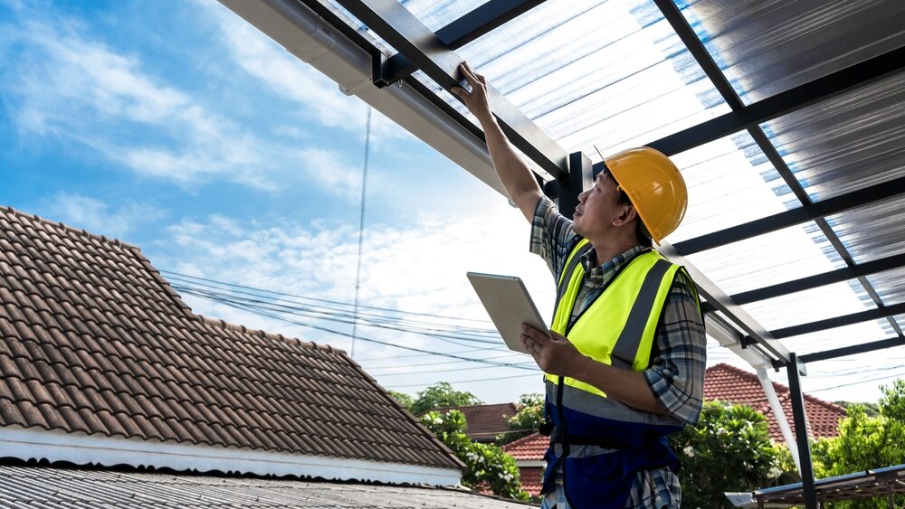 A roofer holds a tablet while inspecting a house roof.